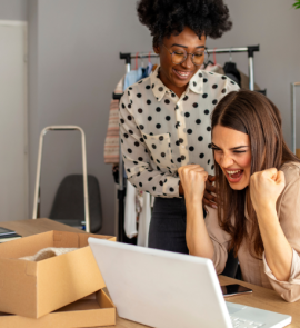 Two people, one Black and one white, celebrate around a computer.