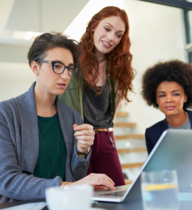 Three people, two white and one Black, talk around a computer screen.